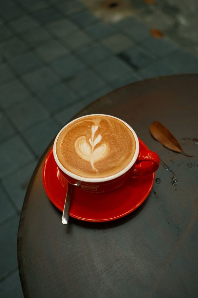 A beautifully crafted latte with heart-shaped art in a red cup on an outdoor table.